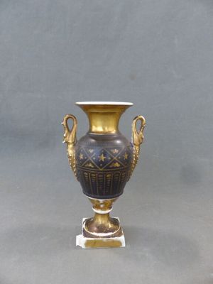 un vase doré et noir posé sur un socle, sur fond gris