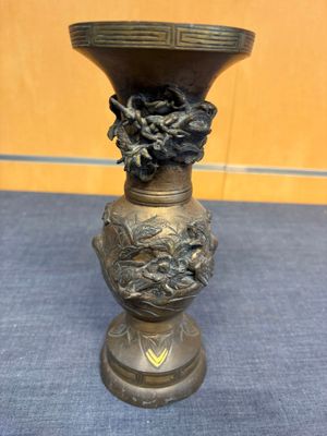 vase en laiton orné d'un visage sur sa base, posé sur un tapis bleu