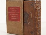an old book with a red cover sitting on top of a white table