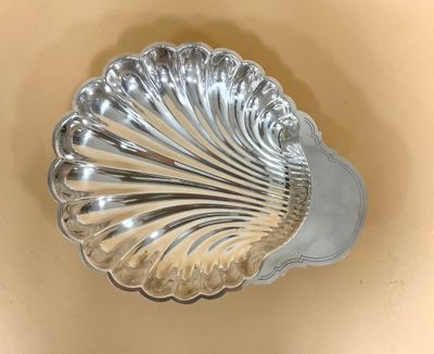 un plat argenté en forme de coquillage posé sur un fond beige