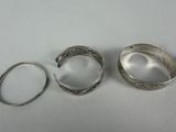 three silver bracelets and a ring on a white surface