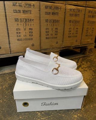 La boîte à chaussures est remplie de chaussures blanches ornées d'une boucle dorée.