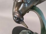 a bronze sculpture of a bird flying over a leaf