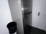 a silver refrigerator and a trash can in the corner of a room