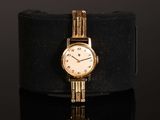 an image of a gold wrist watch with roman numerals on a black surface