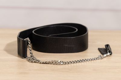 une ceinture en cuir noir avec une chaîne en argent posée sur une table en bois