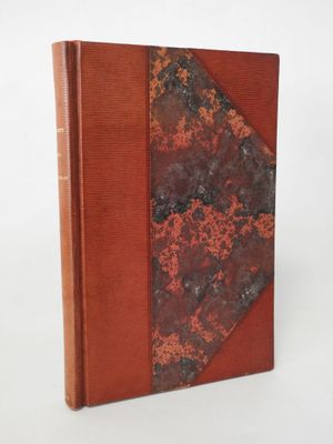 an old book with a red cover sitting on top of a white surface