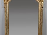 une image représentant un miroir à cadre doré posé contre un mur blanc