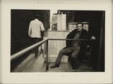 photographie en noir et blanc d'un homme assis sur un banc près d'une balustrade