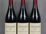 trois bouteilles de vin rouge sont posées sur une table en verre