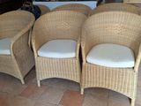 Trois fauteuils en osier avec des coussins sont disposés sur le carrelage du salon.