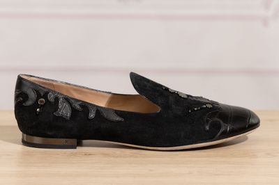Le mocassin noir est posé sur une table en bois, avec un mur blanc en arrière-plan.