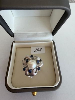 a ring in a box that has a pearl and blue stones in it