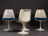 three white tulip chairs with blue cushions sit in a row
