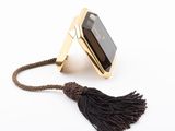 the gold ring with a black stone and a tassel on a white background