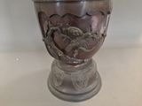 a silver vase with a bird on it sitting on a table