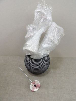 un vase noir recouvert d'un film plastique, à côté d'une aiguille