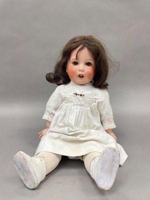 une poupée ancienne en porcelaine, assise par terre, vêtue d'une robe blanche