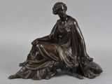 une statue antique en bronze représentant une femme assise sur un rocher