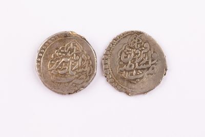 two silver coins with arabic writing on them on a white surface