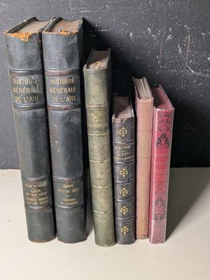Plusieurs vieux livres sont alignés sur une étagère devant un tableau noir.