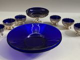 un saladier en verre bleu et six tasses en argent posés sur une table
