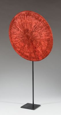 a red sculpture on a black stand with a gray background