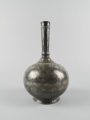 un vieux vase en argent muni d'une anse noire, posé sur une surface blanche