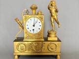 une horloge en or surmontée d'une statue, à côté d'une paire de ciseaux