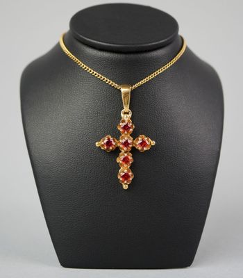 un collier en or avec un pendentif en forme de croix rouge sur un mannequin noir