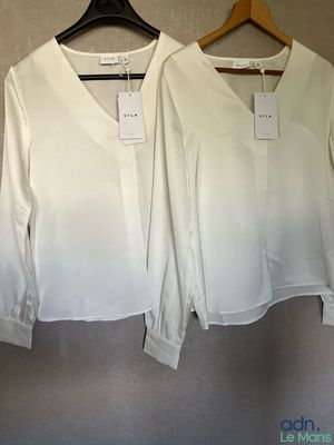 pair of white blouses hanging on a hanger in a clothing store