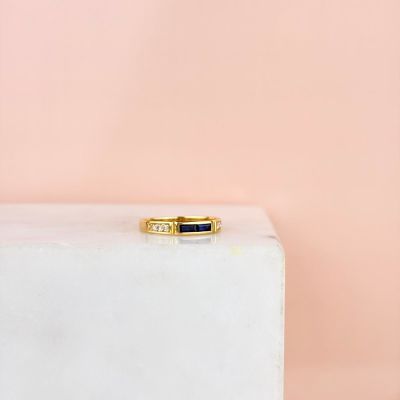 une bague en or ornée de deux pierres noires, posée sur un bloc de marbre blanc