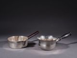 pair of silver saucepans with wooden handles on a grey background