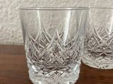 two crystal tumblers on a wooden table with a white wall in the background