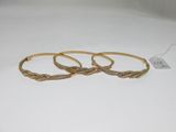 three gold bracelets on a white surface with a price tag