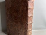 an old brown book sitting on top of a table next to a white wall