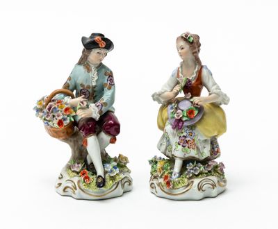 two figurines of a man and a woman with baskets of flowers