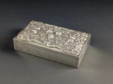 une boîte ancienne en argent, ornée de fleurs et de feuilles sur un fond noir