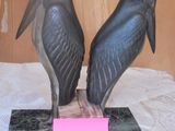 two statues of birds sitting on a table with a pink note