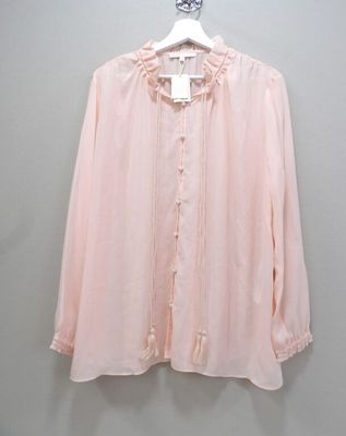 the pink blouse is hanging on a hanger against a wall