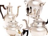 three silver teapots and two silver cups on a white background