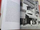 Quelqu'un tient un livre ouvert sur une table, avec une photo d'un bâtiment en arrière-plan.