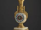 un vase décoré, doré et blanc, surmonté d'une horloge