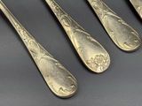 quatre cuillères en argent ornées de motifs, posées sur une table