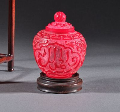 un vase rouge posé à côté d'une chaise sur une surface grise