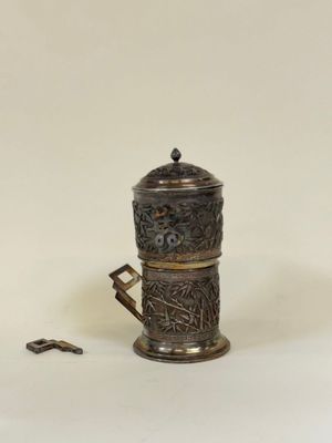 une petite cafetière en argent avec une anse, posée sur une surface blanche