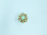 a close up of a turquoise and gold ring on a white surface