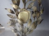 a gold clock on a stand with leaves on it