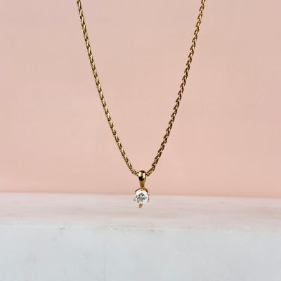 a gold chain necklace with a single diamond on a pink background