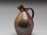 un vase marron muni d'une anse marron, posé sur une surface blanche